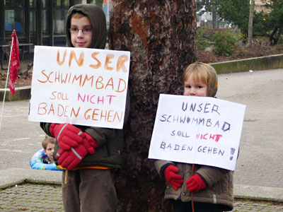 Zwei Kinder halten Plakate: Unser Schwimmbad soll nicht baden gehen!