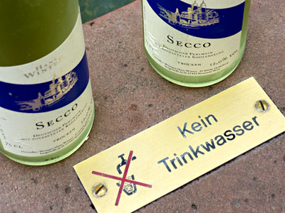 Zwei Proseccoflaschen vor dem Schild „Kein Trinkwasser”