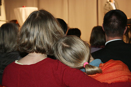 Ein Mädchen lehnt sich an die Schulter seiner Mutter. Beide blicken auf die Bühne.